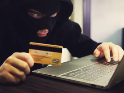 W2M8KX Man in robber mask and hood misappropriates personal bank data. Cyber fraudster attacks online banking system. Hacker makes financial fraud via