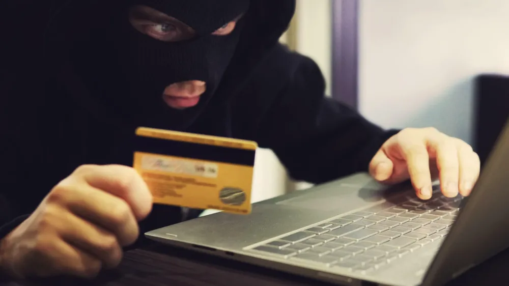 W2M8KX Man in robber mask and hood misappropriates personal bank data. Cyber fraudster attacks online banking system. Hacker makes financial fraud via