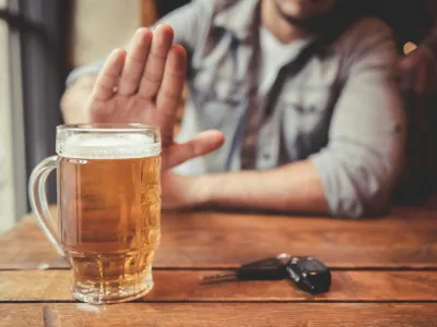 Do not drink and drive! Cropped image of man showing stop gesture and refusing to drink beer. Car keys lying near