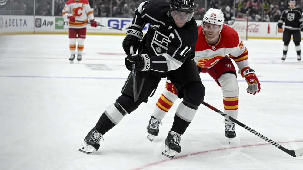 Los Angeles Kings center Anze Kopitar, left, controls the puck next to Calgary Flames center Blake Coleman during the second period of an NHL hockey game in Los Angeles, Saturday, Dec. 23, 2023. (AP Photo/Alex Gallardo)