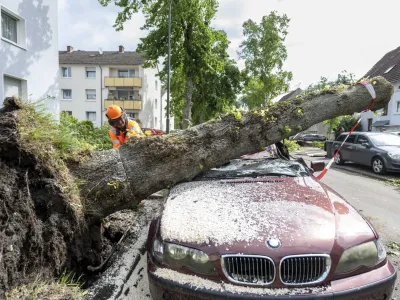 A worker removes a fallen free that fell on a car in Lippstadt, Germany, a day after heavy rains and a tornado hit the area, Saturday, May 21, 2022. (David Inderlied/dpa via AP)