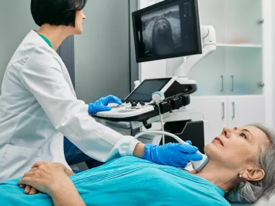 Ultrasound diagnostics of thyroid gland. Endocrinologist making ultrasonography to senior female patient at ultrasound office of medical clinic