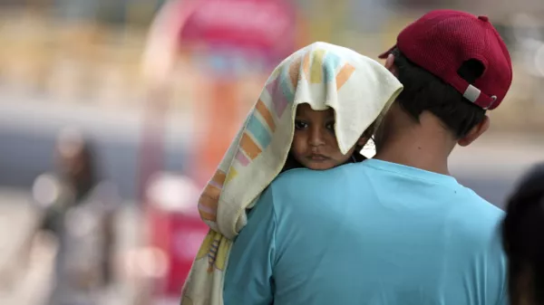 A man carries a child with its head covered with a towel to protect it from the heat in Jammu, India, Sunday, June 2, 2024. (AP Photo/Channi Anand)