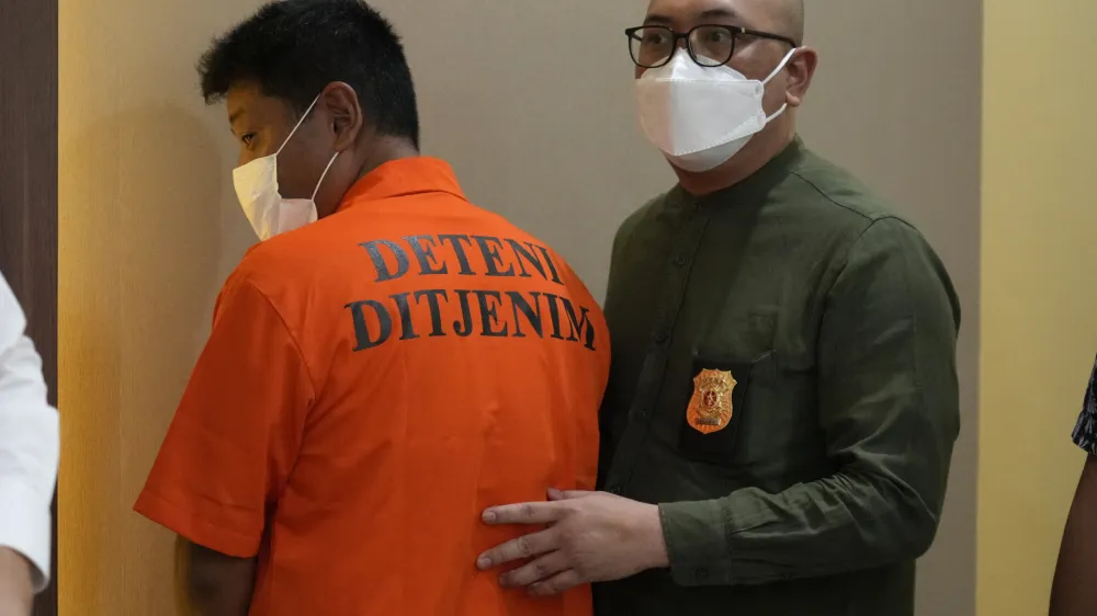 Immigration officers escort Mitsuhiro Taniguchi, 47, of Japan, left, during a press conference at immigration office in Jakarta, Indonesia Wednesday, June 8, 2022. Authorities on the southern tip of Indonesia's Sumatra island arrested a Japanese fugitive accused of fraud in Japan in connection with the receipt of a massive amount of COVID-19 subsidies for small businesses in distress, police said Wednesday.(AP Photo/Achmad Ibrahim)