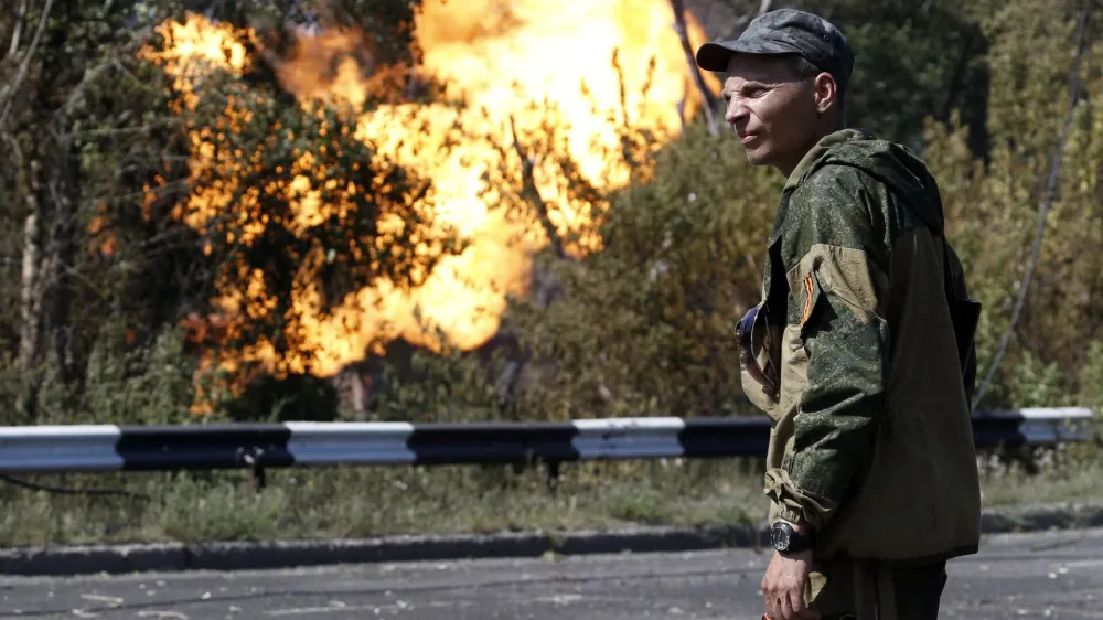 An armed pro-Russian separatist looks as flames erupt from a gas pipeline after a shelling in Donetsk, August 15, 2014. EUTERS/Sergei Karpukhin (UKRAINE - Tags: ENERGY POLITICS CIVIL UNREST CONFLICT MILITARY)