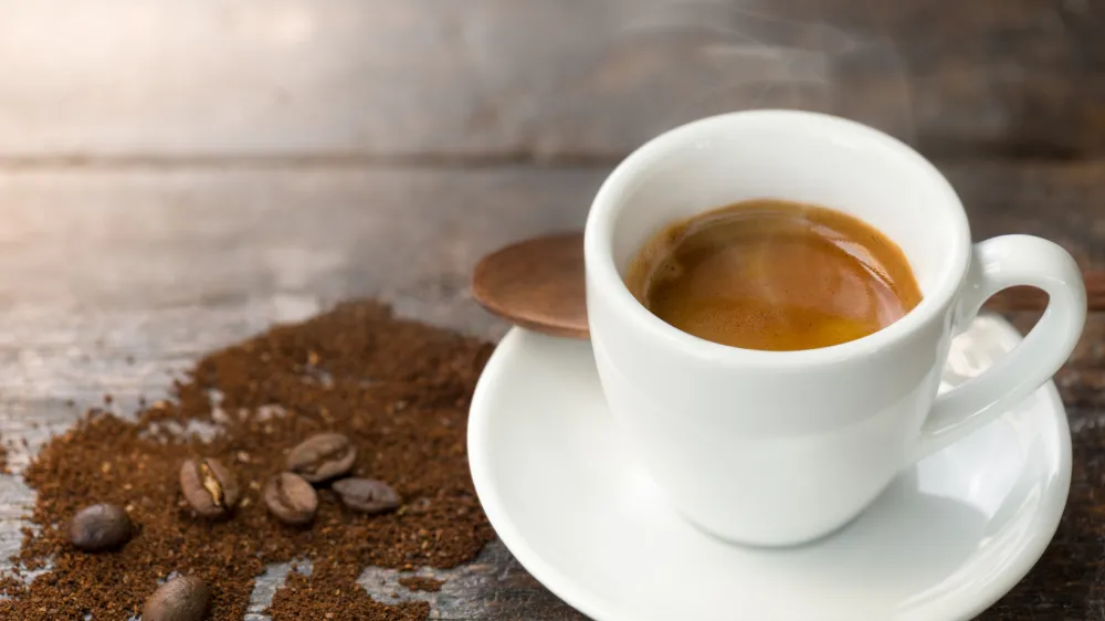 Espresso and coffee beans. Cup of hot espresso on wooden table with smoke.