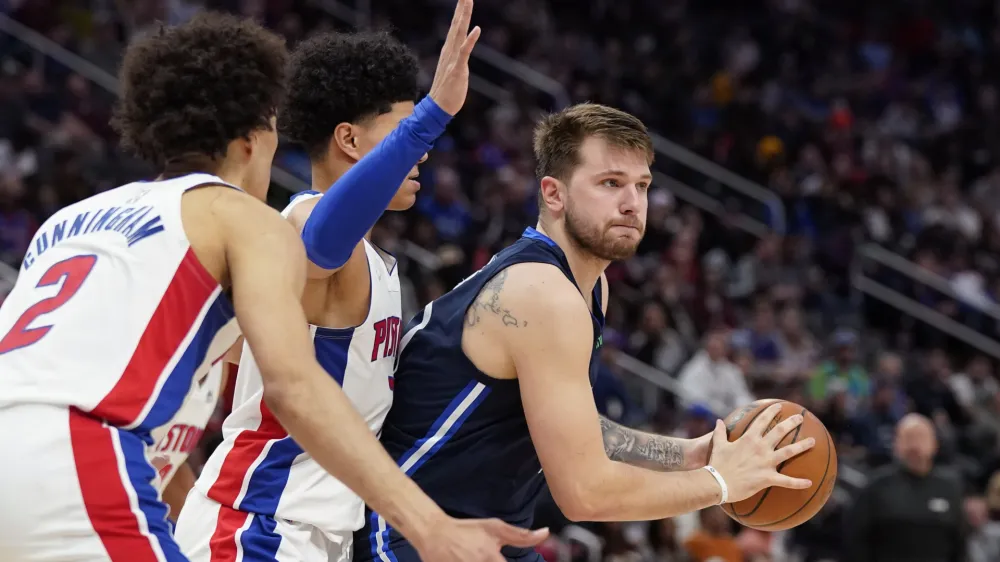 Dallas Mavericks guard Luka Doncic (77) looks to pass as Detroit Pistons guard Killian Hayes, center, and guard Cade Cunningham (2) defend during the second half of an NBA basketball game, Wednesday, April 6, 2022, in Detroit. (AP Photo/Carlos Osorio)
