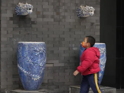 A child wearing a mask wears near water fountain featuring dragons on Thursday, April 28, 2022, in Beijing. With the May Day holidays just around the corner, Beijing has been tightening COVID-19 restrictions as it seeks to prevent a wider outbreak. (AP Photo)