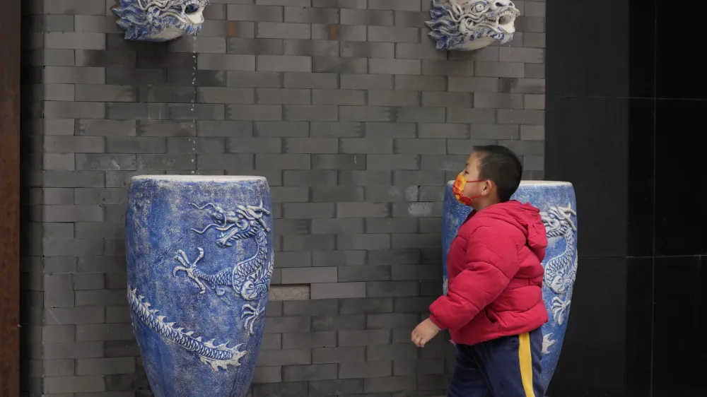 A child wearing a mask wears near water fountain featuring dragons on Thursday, April 28, 2022, in Beijing. With the May Day holidays just around the corner, Beijing has been tightening COVID-19 restrictions as it seeks to prevent a wider outbreak. (AP Photo)