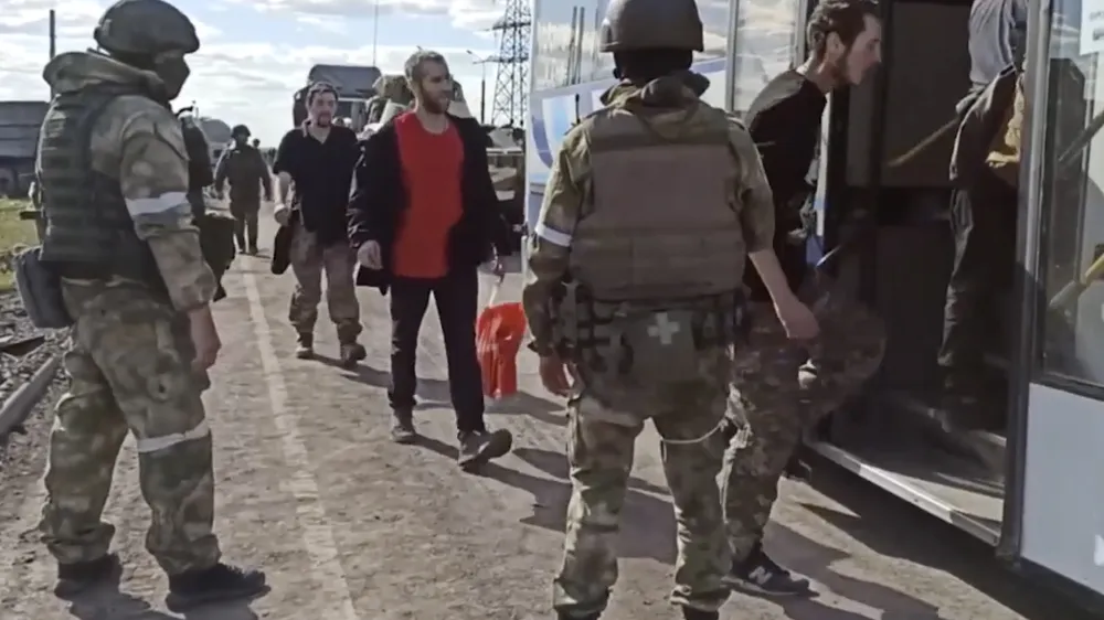 In this photo taken from video released by the Russian Defense Ministry Press Service on Tuesday, May 17, 2022, Russian servicemen watch Ukrainian servicemen boarding a bus as they are being evacuated from the besieged Azovstal steel plant in Mariupol, Ukraine. More than 260 fighters, some severely wounded, were pulled from a steel plant on Monday that is the last redoubt of Ukrainian fighters in the city and transported to two towns controlled by separatists, officials on both sides said. (Russian Defense Ministry Press Service via AP)