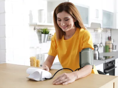 Woman checking blood pressure with sphygmomanometer at table indoors. Cardiology concept