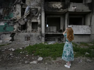 A woman takes pictures of a building destroyed by shelling, in Borodyanka, on the outskirts of Kyiv, Ukraine, Saturday, June 4, 2022. (AP Photo/Natacha Pisarenko)