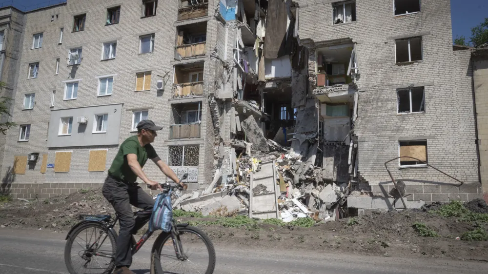 A man rides a bicycle past a building damaged in Russian shelling in Bakhmut, Donetsk region, Ukraine, Monday, June 20, 2022. (AP Photo/Efrem Lukatsky)