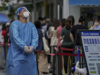 A worker in protective gears reacts as residents line up at a testing site due to requirements for a negative COVID test in the last 72 hours to enter some buildings and using public transportation in Beijing, Monday, July 4, 2022. (AP Photo/Andy Wong)