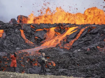 People look at the lava flowing on Fagradalsfjall volcano in Iceland on Wednesday Aug. 3, 2022, which is located 32 kilometers (20 miles) southwest of the capital of Reykjavik and close to the international Keflavik Airport. Authorities in Iceland say the volcano in the southwest of the country is erupting just eight months after its last eruption officially ended. (AP Photo/Marco Di Marco)