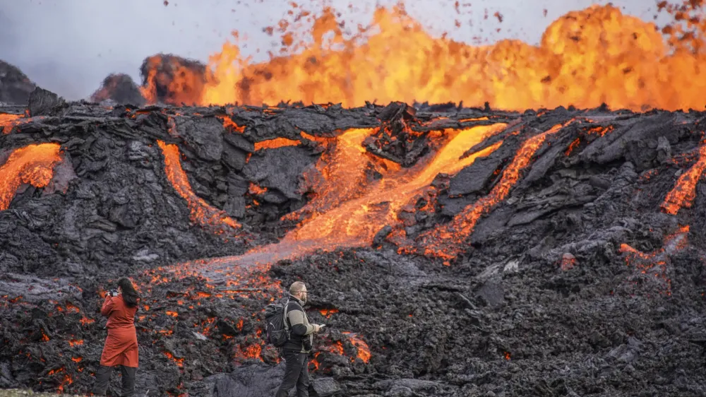 People look at the lava flowing on Fagradalsfjall volcano in Iceland on Wednesday Aug. 3, 2022, which is located 32 kilometers (20 miles) southwest of the capital of Reykjavik and close to the international Keflavik Airport. Authorities in Iceland say the volcano in the southwest of the country is erupting just eight months after its last eruption officially ended. (AP Photo/Marco Di Marco)