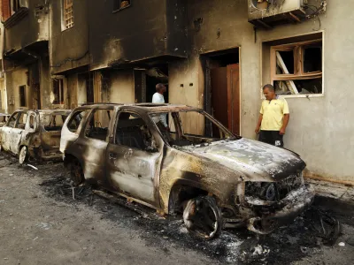 Men survey the remains of cars burned during clashes on a street in the Libyan capital of Tripoli, Sunday, August 28 2022. Deadly clashes broke out Saturday in Libya's capital between militias backed by its two rival administrations, portending a return to violence amid a long political stalemate. (AP Photo/Yousef Murad)