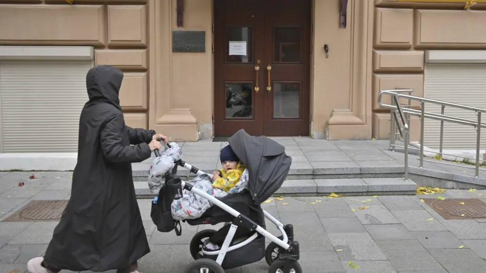 A woman pushes a baby on a stroller past the entrance to human rights group Memorial's office, in Moscow, Russia, Friday, Oct. 7, 2022. On Friday, Oct. 7, 2022 the Nobel Peace Prize was awarded to jailed Belarus rights activist Ales Bialiatski, the Russian group Memorial and the Ukrainian organization Center for Civil Liberties. (AP Photo/Dmitry Serebryakov)