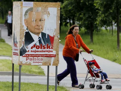REFILE - ADDING BYLINE<br><br>A woman and a toddler pass by an election poster of Jaroslaw Kaczynski, presidential candidate of Poland's Law and Justice Party (PiS) and twin brother of the late president Lech Kaczynski, in Warsaw June 16, 2010. Poland will choose a new president on June 20 in an election brought forward from the autumn after the death of conservative incumbent Lech Kaczynski in a plane crash. REUTERS/Peter Andrews (POLAND - Tags: POLITICS ELECTIONS)