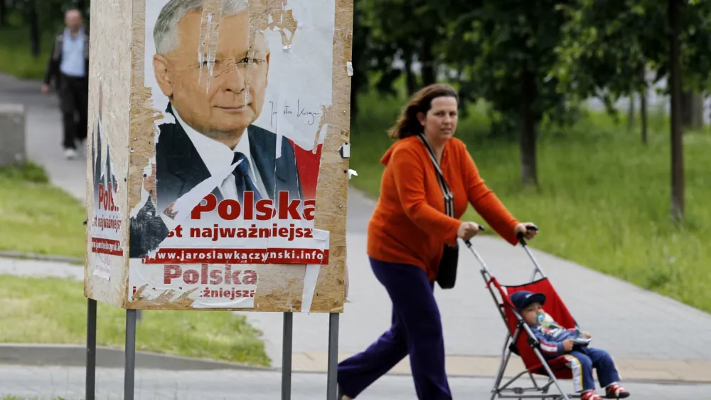 REFILE - ADDING BYLINE<br><br>A woman and a toddler pass by an election poster of Jaroslaw Kaczynski, presidential candidate of Poland's Law and Justice Party (PiS) and twin brother of the late president Lech Kaczynski, in Warsaw June 16, 2010. Poland will choose a new president on June 20 in an election brought forward from the autumn after the death of conservative incumbent Lech Kaczynski in a plane crash. REUTERS/Peter Andrews (POLAND - Tags: POLITICS ELECTIONS)