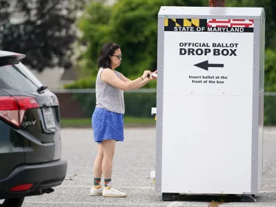 FILE - A woman drops a ballot into a drop box while casting her vote during Maryland's primary election, Tuesday, July 19, 2022, in Baltimore.  On Friday, Nov. 11, The Associated Press reported on stories circulating online incorrectly claiming a candidate winning an election with a majority of mailed ballots is proof of fraud. (AP Photo/Julio Cortez, File)