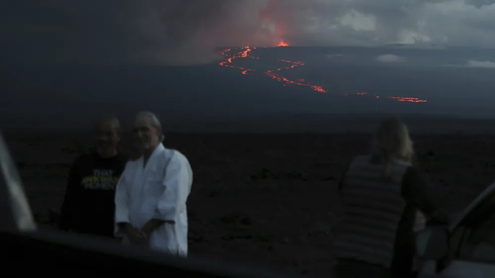 Spectators take photos as they watch the lava flow down the mountain from the Mauna Loa eruption, Tuesday, Nov. 29, 2022, near Hilo, Hawaii. (AP Photo/Marco Garcia)