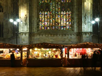 Milan, Italy - December 25, 2015: Christmas market in Piazza del Duomo in late evening. Behind the stalls there is the gothic cathedral with the stained-glass windows lighted for the festivity. Some people are visible in the square.