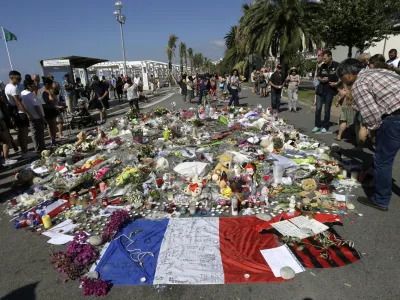 FILE - People look at flowers placed on the Promenade des Anglais at the scene of a truck attack Monday July 18, 2016 in Nice, southern France. A French court on Tuesday Dec.13, 2022 convicted eight people charged in connection with a truck attack more than six years ago by an Islamic State sympathizer that killed 86 people celebrating Bastille Day in the French Riviera city of Nice. (AP Photo/Claude Paris, File)