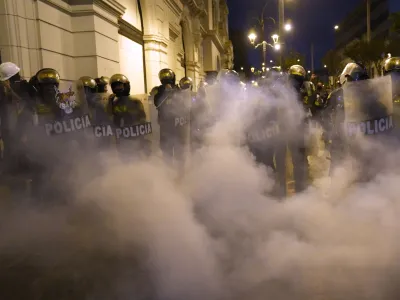 Riot police officers stand guard before clouds of tear gas after clashes with supporters of ousted Peruvian President Pedro Castillo, in Lima, Peru, Thursday, Dec. 15, 2022. A Peruvian judge on Thursday ordered Castillo to remain in custody for 18 months, approving a request from authorities for time to build their rebellion case against him. (AP Photo/Martin Mejia)