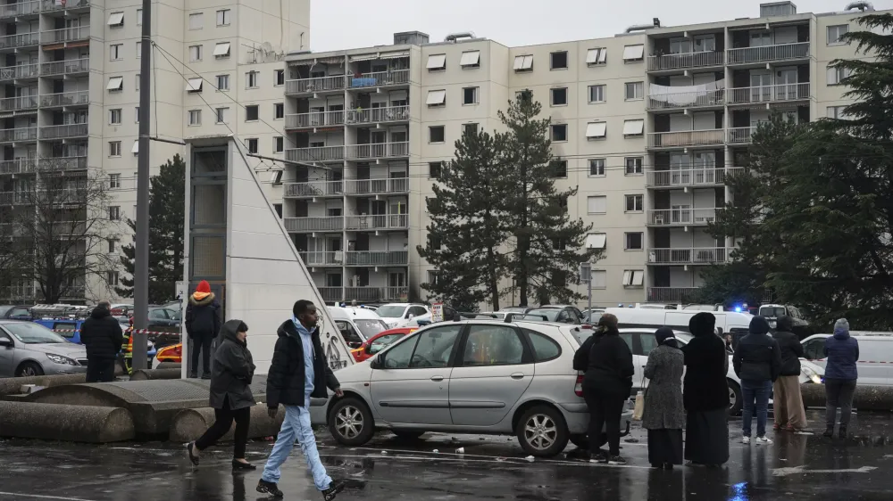 Onlookers stand next to apartment buildings seen in background at Le Mas du Taureau neighborhood, in Vaulx en Velin, outside Lyon, central France, Friday, Dec. 16, 2022. French authorities say 10 people including five children died in a fire in an apartment building outside the city of Lyon. The cause of the fire is being investigated. (AP Photo/Laurent Cipriani)