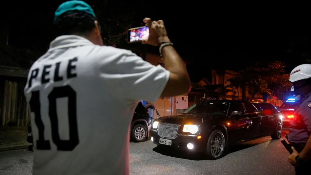 A fan wearing a shirt with Brazilian soccer legend Pele's name on it, records images as a vehicle transports Pele's body, near the Vila Belmiro stadium in Santos, Brazil, January 2, 2023. REUTERS/Diego Vara