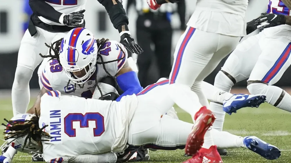 CLARIFIES THAT IMAGE SHOWN IS FROM THE END OF A TACKLE SECONDS BEFORE HAMLIN COLLAPSED - Buffalo Bills safety Damar Hamlin (3) lies on the turf after making a tackle on Cincinnati Bengals wide receiver Tee Higgins, who is blocked from view, as Buffalo Bills linebacker Tremaine Edmunds (49) assists at the end of the play during the first half of an NFL football game between the Cincinnati Bengals and the Buffalo Bills, Monday, Jan. 2, 2023, in Cincinnati. After getting up from the play, Hamlin collapsed and was administered CPR on the field. (AP Photo/Joshua A. Bickel)