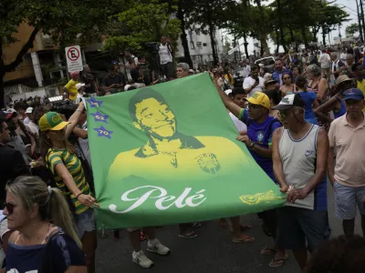 People hold a banner of the late Brazilian soccer great Pele along the route of his funeral procession from Vila Belmiro stadium to the cemetery in Santos, Brazil, Tuesday, Jan. 3, 2023. (AP Photo/Matias Delacroix)