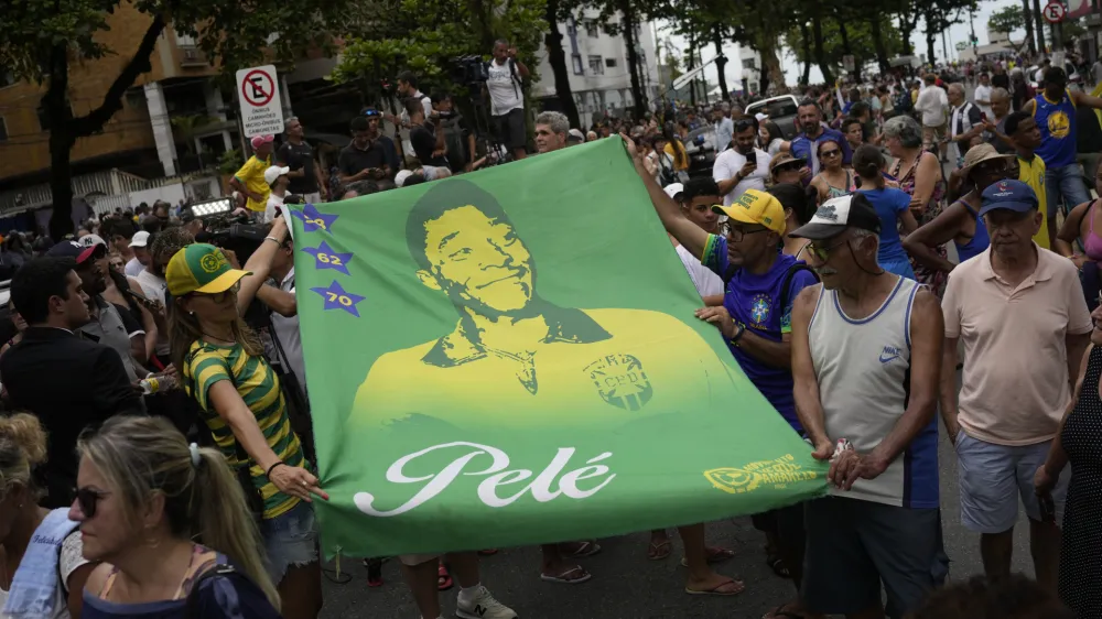 People hold a banner of the late Brazilian soccer great Pele along the route of his funeral procession from Vila Belmiro stadium to the cemetery in Santos, Brazil, Tuesday, Jan. 3, 2023. (AP Photo/Matias Delacroix)