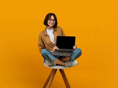 Website advertisement. Happy young lady with laptop showing empty computer screen recommending online service, sitting in chair over yellow wall background. Mockup