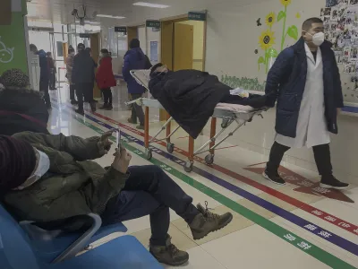 A man browses his smartphone as an elderly patient is wheeled to an emergency hall in a hospital in Beijing, Saturday, Jan. 7, 2023. China has suspended or closed the social media accounts of more than 1,000 critics of the government's policies on the COVID-19 outbreak, as the country moves to further open up. (AP Photo/Andy Wong)