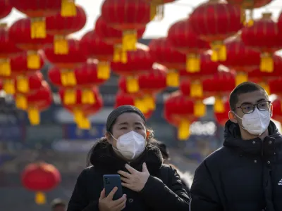 Visitors wearing face masks walk under a row of decorative lanterns for the upcoming Lunar New Year at a tourist shopping street in Beijing, Saturday, Jan. 21, 2023. The Year of the Rabbit officially begins on Sunday. (AP Photo/Mark Schiefelbein)