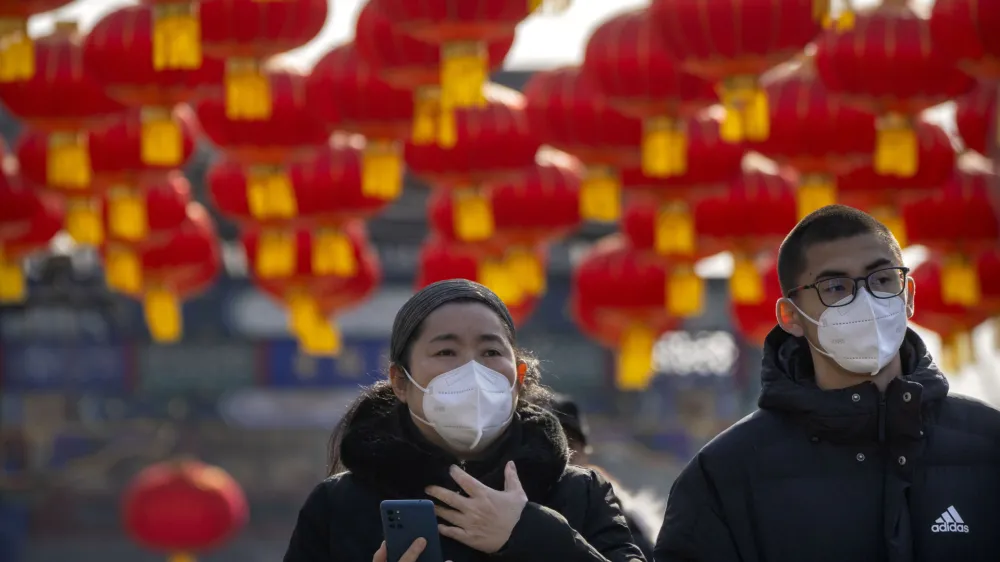 Visitors wearing face masks walk under a row of decorative lanterns for the upcoming Lunar New Year at a tourist shopping street in Beijing, Saturday, Jan. 21, 2023. The Year of the Rabbit officially begins on Sunday. (AP Photo/Mark Schiefelbein)