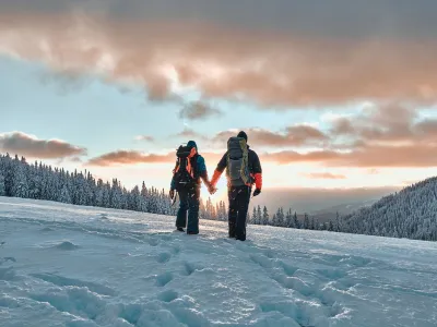 Rest in the mountains. Family couple holding hands and walking in the snowy pine mountains at sunset. The concept of recreation and tourism in winter.