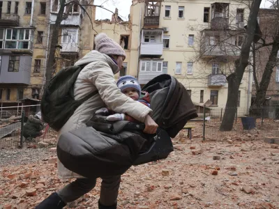 A woman carries her child as they evacuate from a residential building which was hit by a Russian rocket at the city center of Kharkiv, Ukraine, Monday, Jan. 30, 2023. Russian shelling killed at least five people and wounded 13 others during the previous 24 hours, Ukrainian authorities said Monday as the Kremlin's and Kyiv's forces remained locked in combat in eastern Ukraine. (AP Photo/Andrii Marienko)