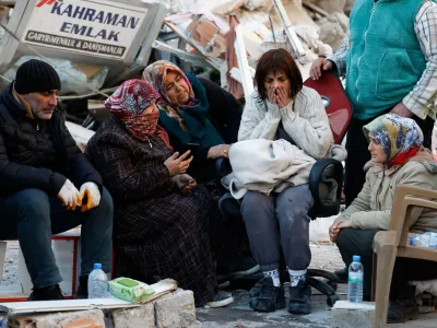 People sit next to rubble at the site of a collapsed building in the aftermath of a deadly earthquake, in Kirikhan, Turkey February 9, 2023. REUTERS/Piroschka van de Wouw