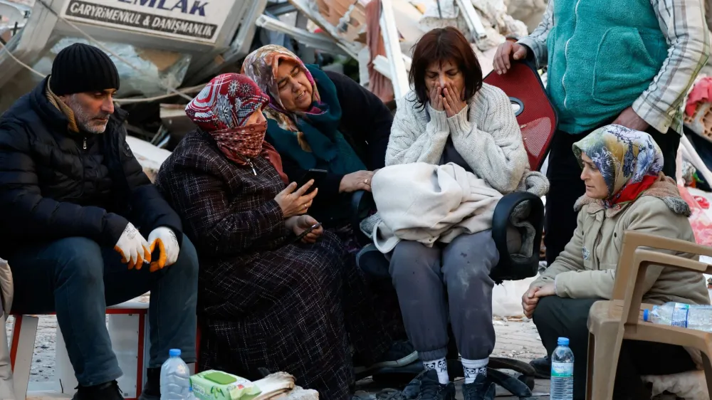 People sit next to rubble at the site of a collapsed building in the aftermath of a deadly earthquake, in Kirikhan, Turkey February 9, 2023. REUTERS/Piroschka van de Wouw