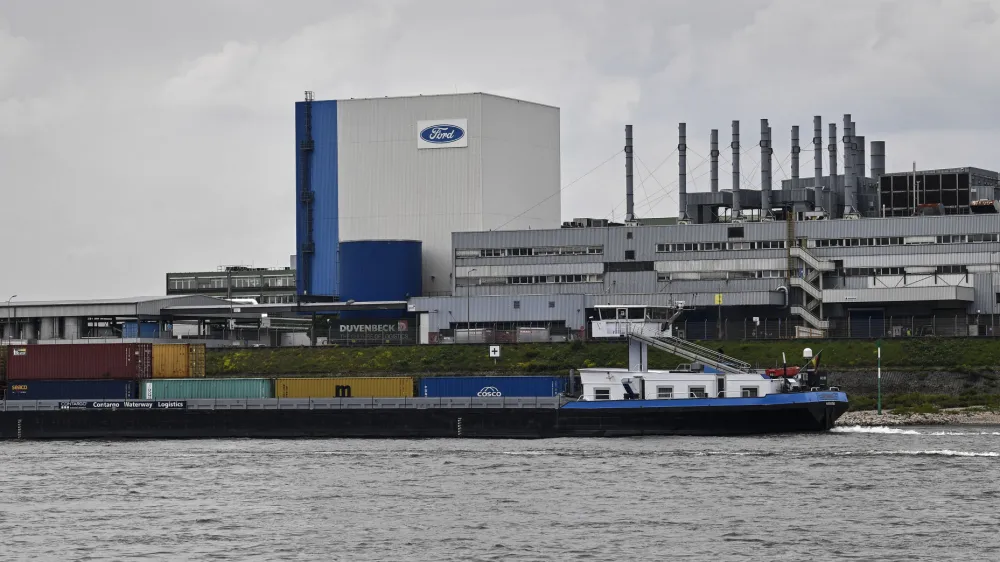 FILE - A container ship passes the Ford car plant in Cologne, Germany, May 4, 2020. Ford said that it will cut 3,800 jobs in Europe over the next three years in an effort to streamline its operations as it contends with economic headwinds and increasing competition on electric cars. The automaker said that 2,300 jobs will go in Germany. (AP Photo/Martin Meissner, File)