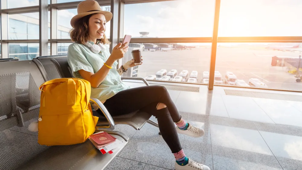 Happy asian woman waiting for her airplane in airport with passport and baggage. Vacation and journey concept