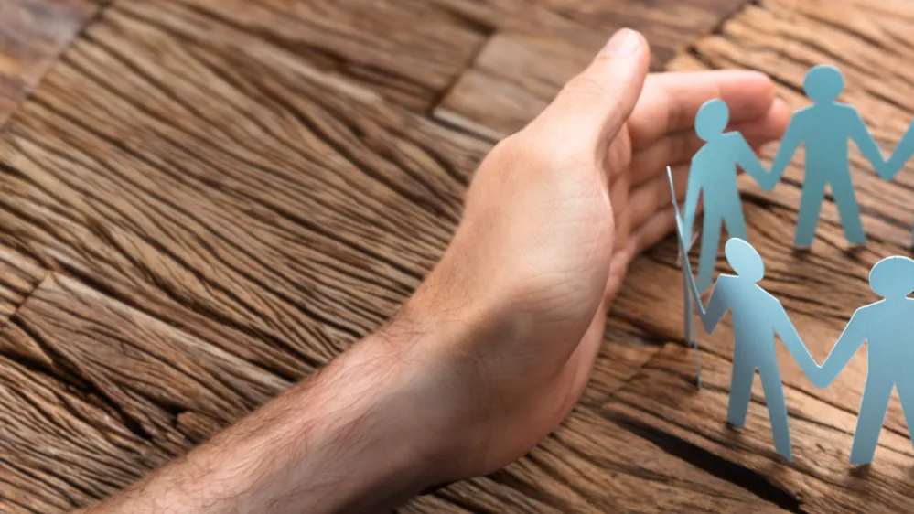 Cropped image of businessman's hands covering paper team on wooden table