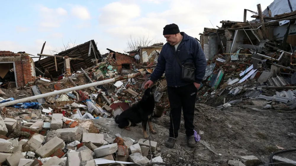 Local resident Volodymyr Alipov, 58, pets a dog among remains of his house destroyed last year by an airstrike during Russia's attack in the village of Tsyrkuny, Kharkiv region, Ukraine March 20, 2023. REUTERS/Sofiia Gatilova