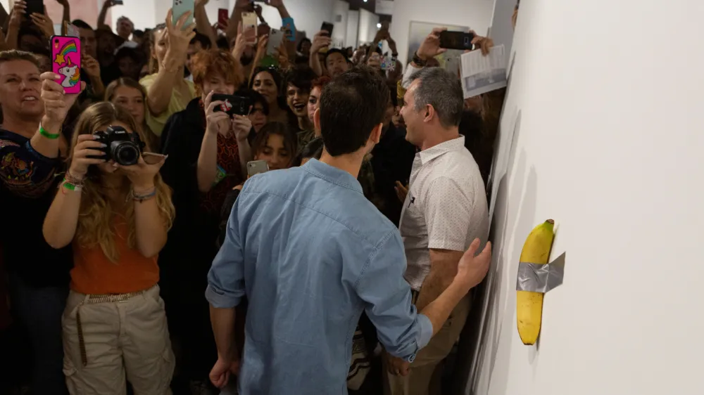 Art Basel visitors use their phones in front of a banana attached with duct-tape that replaces the artwork 'Comedian' by the artist Maurizio Cattelan, which was eaten by David Datuna, in Miami Beach, Florida, December 7, 2019. REUTERS/Eva Marie Uzcategui - RC2NQD93QLIJ