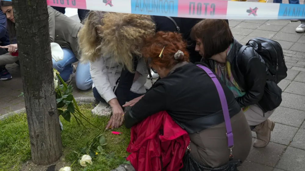 Women lay flowers and light candles for victims near the Vladislav Ribnikar school in Belgrade, Serbia, Wednesday, May 3, 2023. A 13-year-old who opened fire Wednesday at his school in Serbia's capital drew sketches of classrooms and wrote a list of people he intended to target in a meticulously planned attack, police said. (AP Photo/Darko Vojinovic)