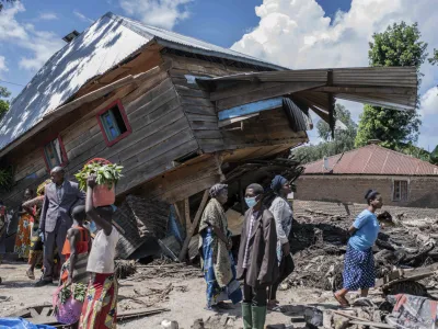 People walk next to a house destroyed by the floods in the village of Nyamukubi, South Kivu province, in Congo, Saturday, May 6, 2023. The death toll from flash floods and landslides in eastern Congo has risen according to the governor and authorities in the country's South Kivu province. (AP Photo/Moses Sawasawa)