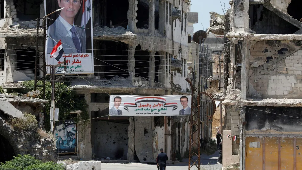 FILE PHOTO: A man walks past banners depicting Syria's President Bashar al-Assad, near damaged buildings, ahead of the May 26 presidential election, in Homs, Syria May 23, 2021. REUTERS/Omar Sanadiki/File Photo